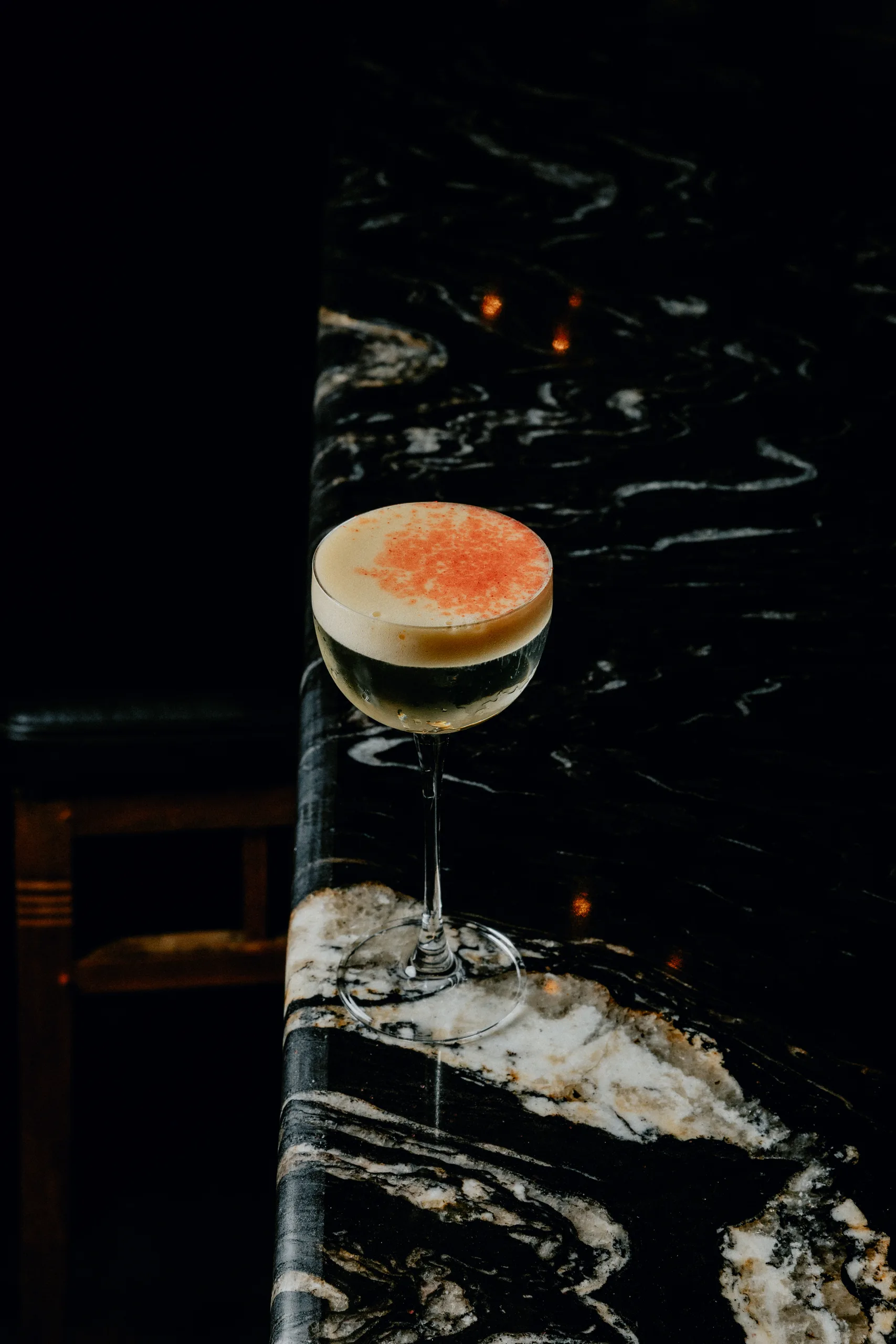 Coupe cocktail with white foam and pink dust on black marble